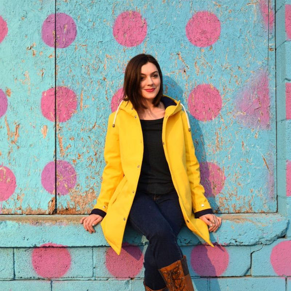 Woman in a yellow Ember & Earth raincoat against a polka-dot wall