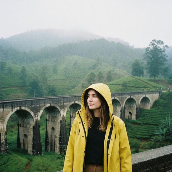 Woman in a yellow Ember & Earth raincoat in front of a stone viaduct